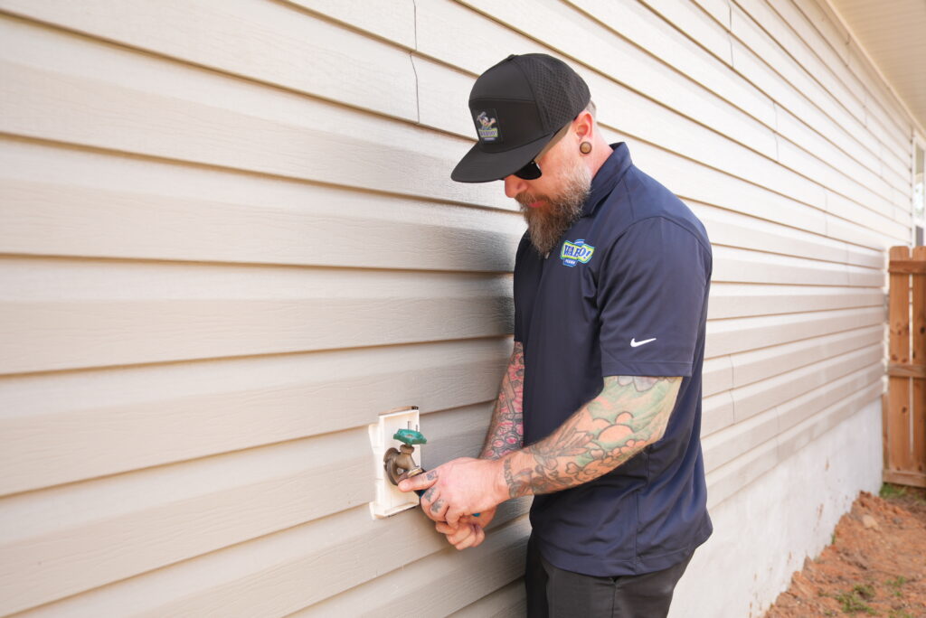 Wahoo Plumbing technician working outside the house, seen wearing a company polo and black cap.